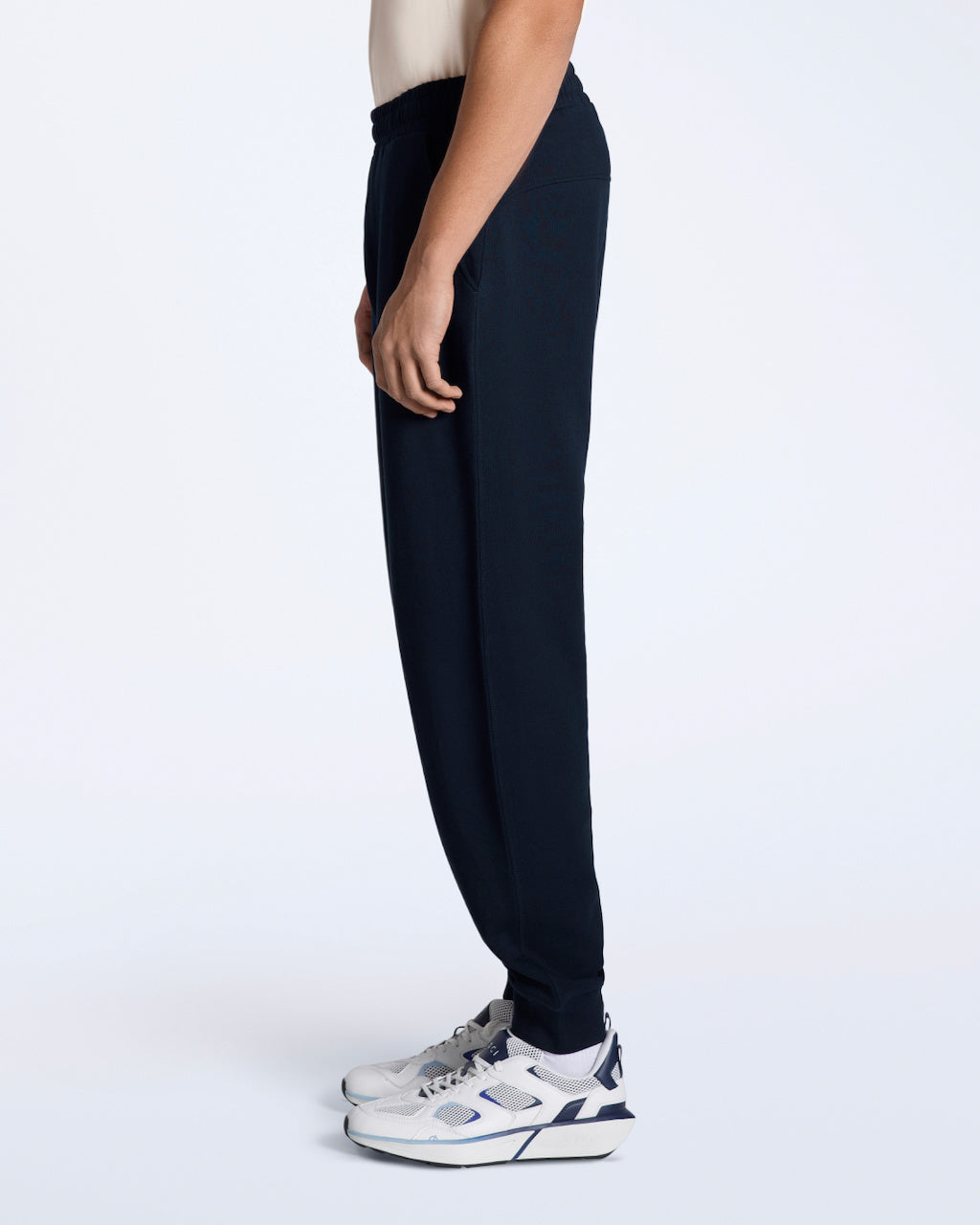 A man facing side on with his arms by his sides, modelling a pair of navy organic cotton joggers.