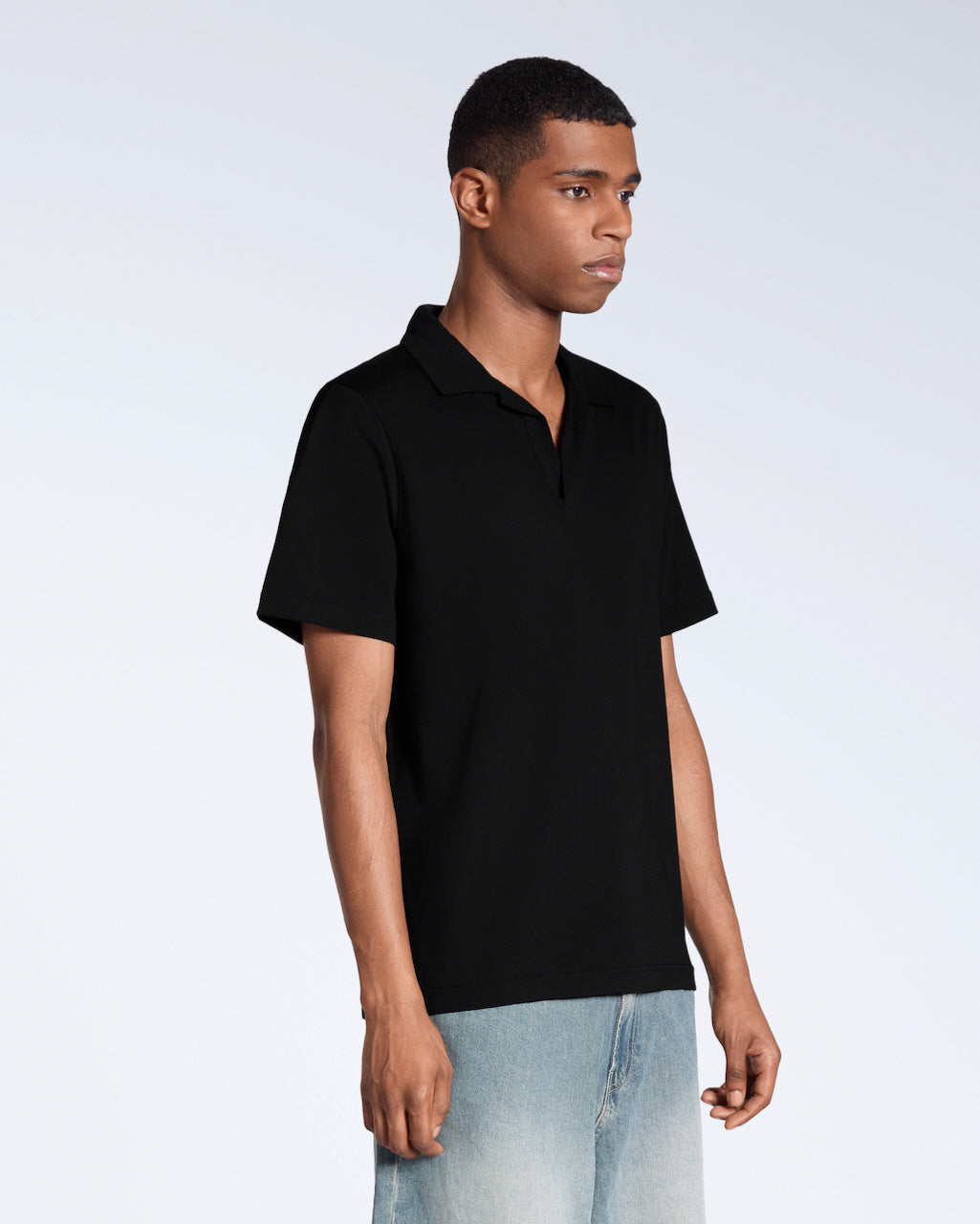 A man at an angle with his arms by his sides, modelling a plain black, short sleeve organic cotton, polo shirt.
