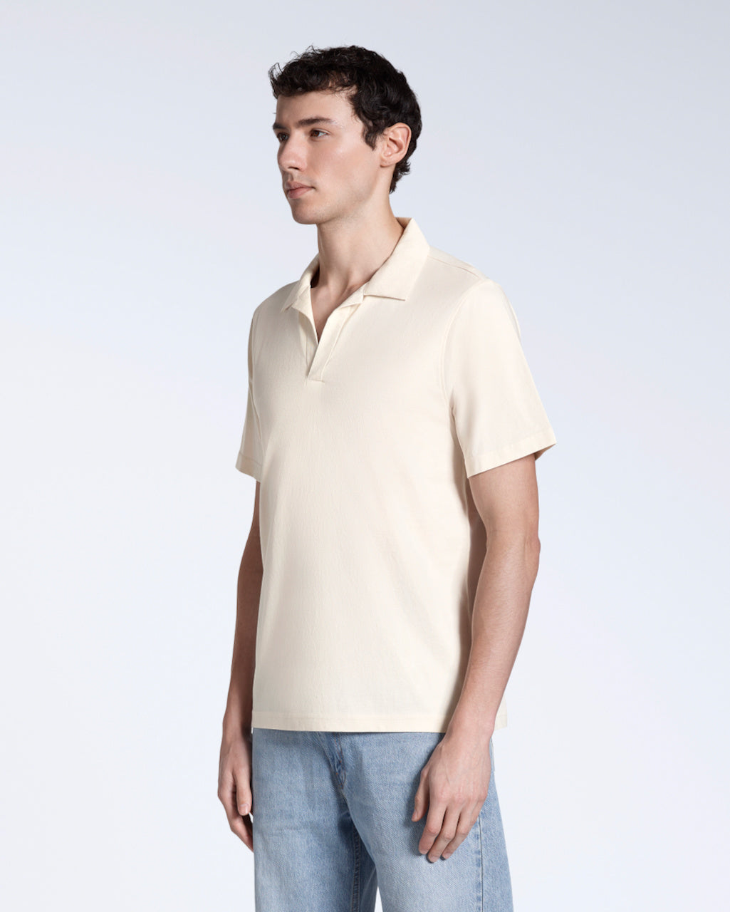 A man at an angle with his arms by his sides, modelling a plain natural coloured, short sleeve organic cotton, polo shirt.