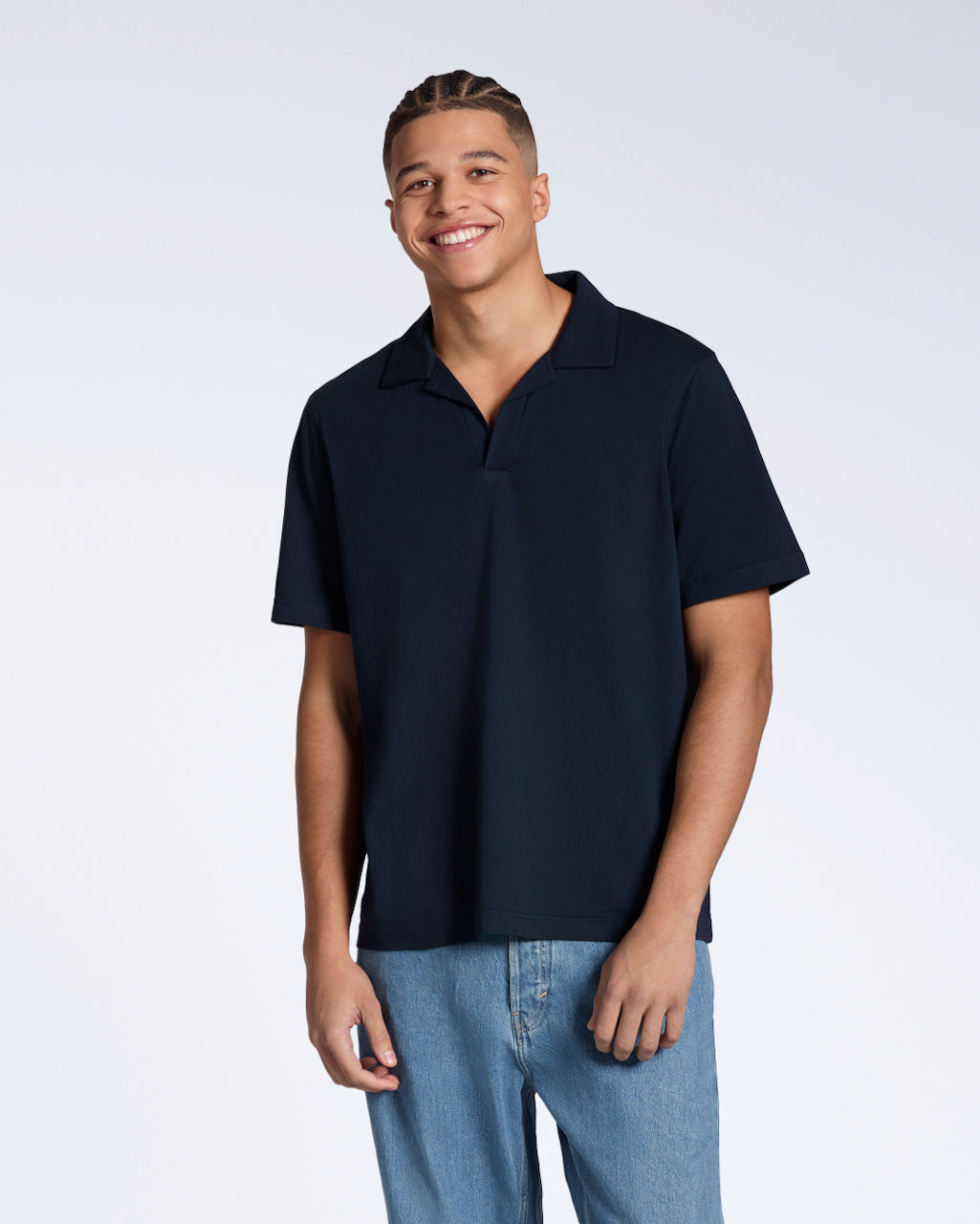 A man smiling into the camera, modelling a plain navy, short sleeve organic cotton polo shirt.