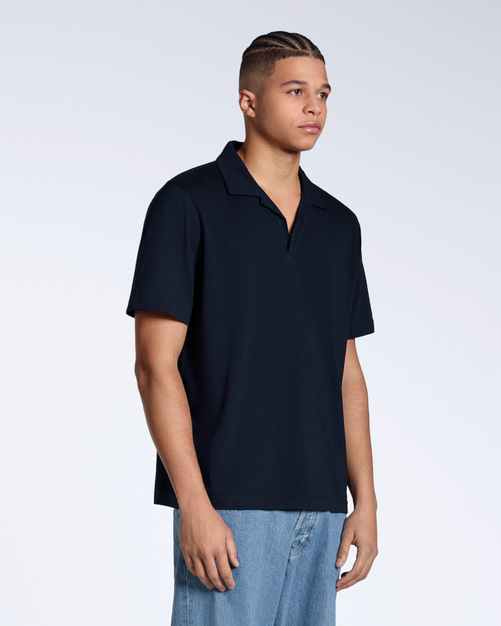A man at an angle with his arms by his sides, modelling a plain navy, short sleeve organic cotton, polo shirt.