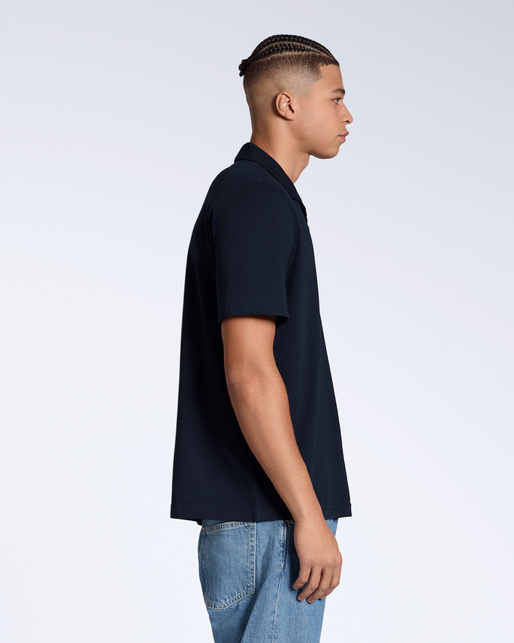 A man facing side on, modelling a plain navy, short sleeve, organic cotton polo shirt.