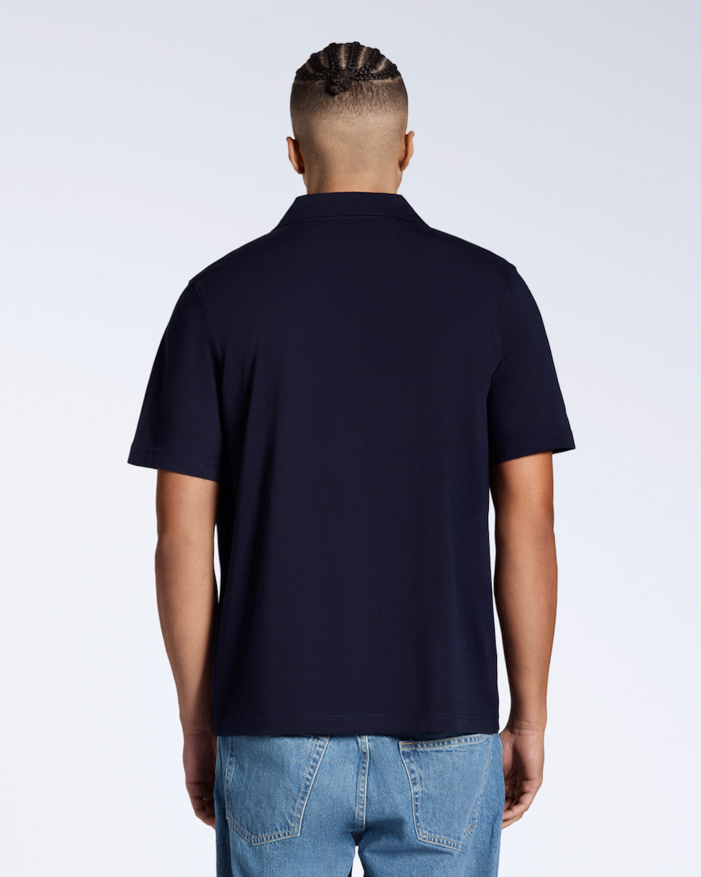 A man facing away from the camera, modelling a plain navy, short sleeve, organic cotton, polo shirt.