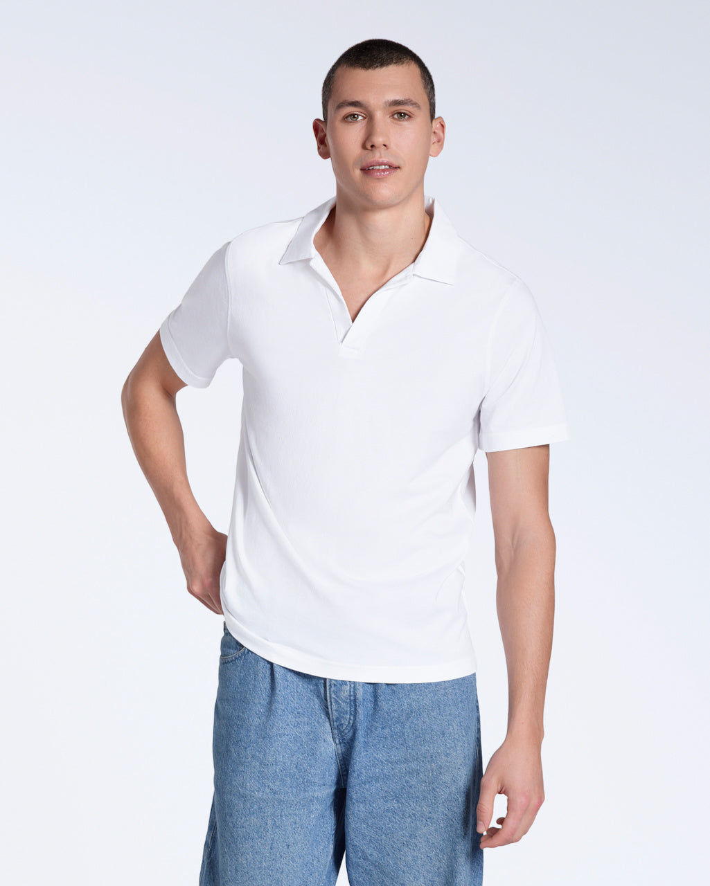 A man looking into the camera, modelling a plain white, short sleeve organic cotton polo shirt.