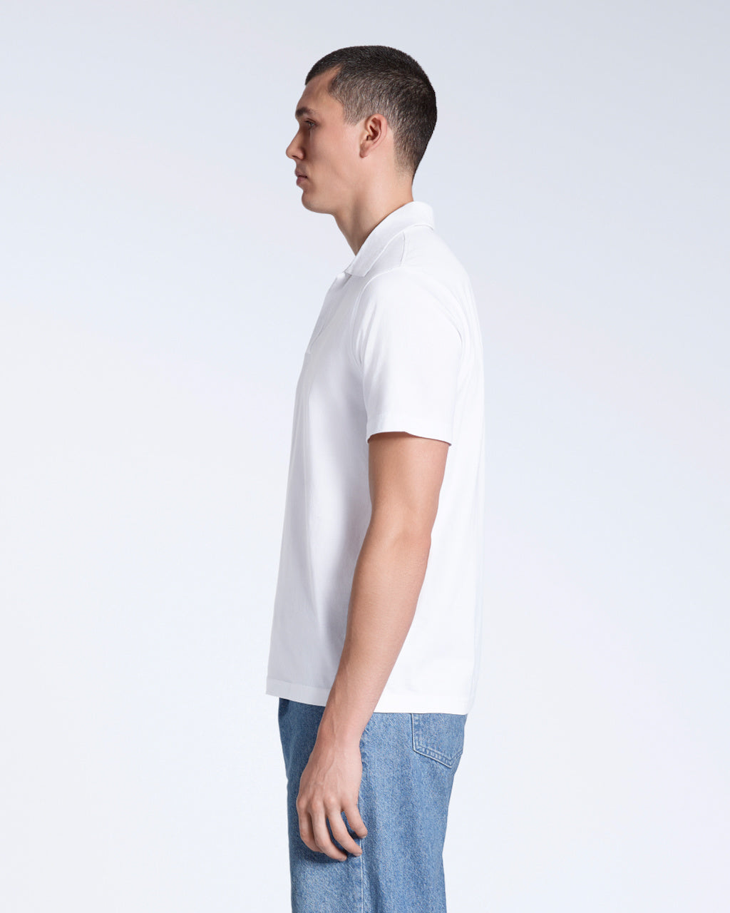 A man facing side on, modelling a plain white, short sleeve organic cotton polo shirt.