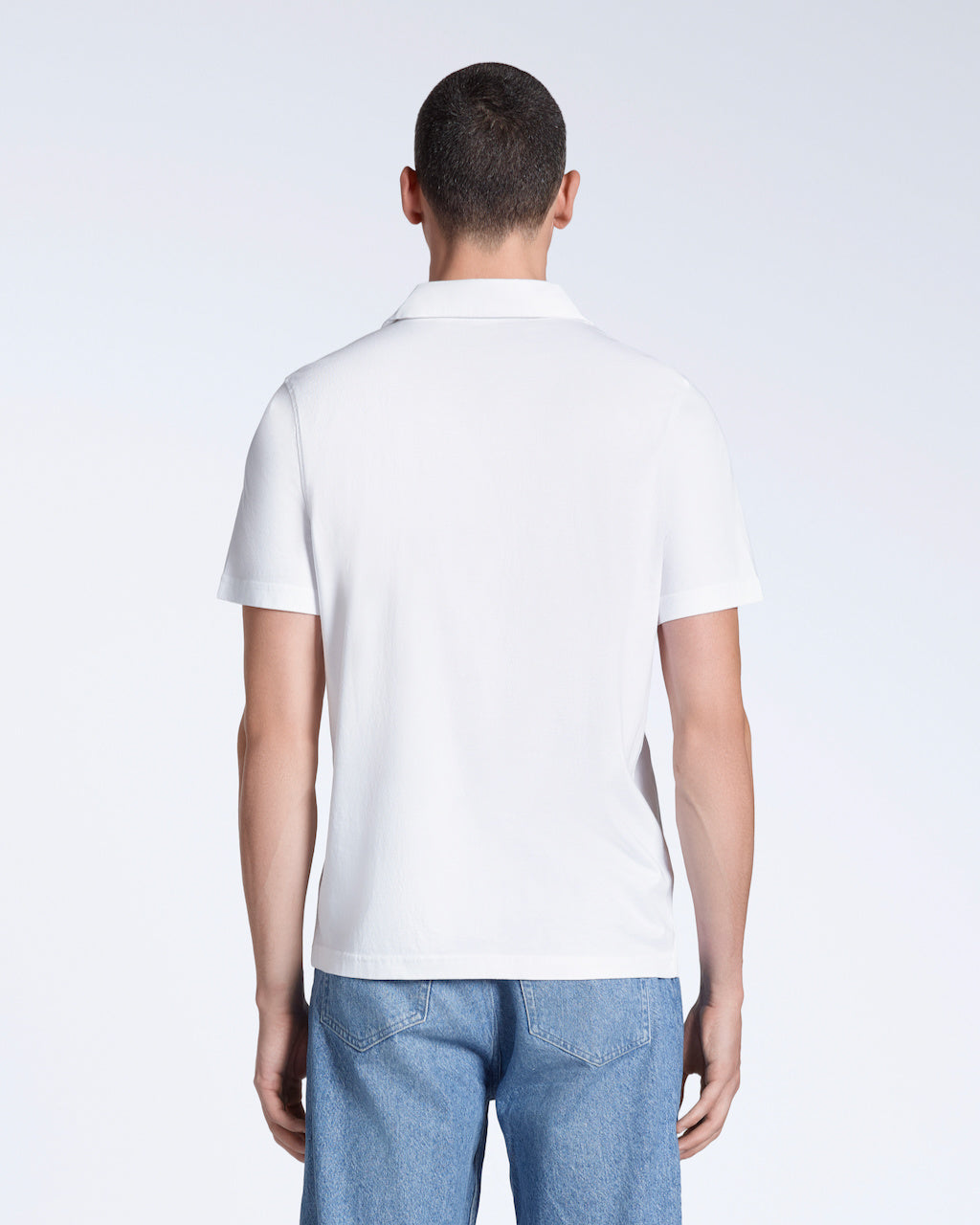 A man facing away from the camera, modelling a plain white, short sleeve organic cotton polo shirt.