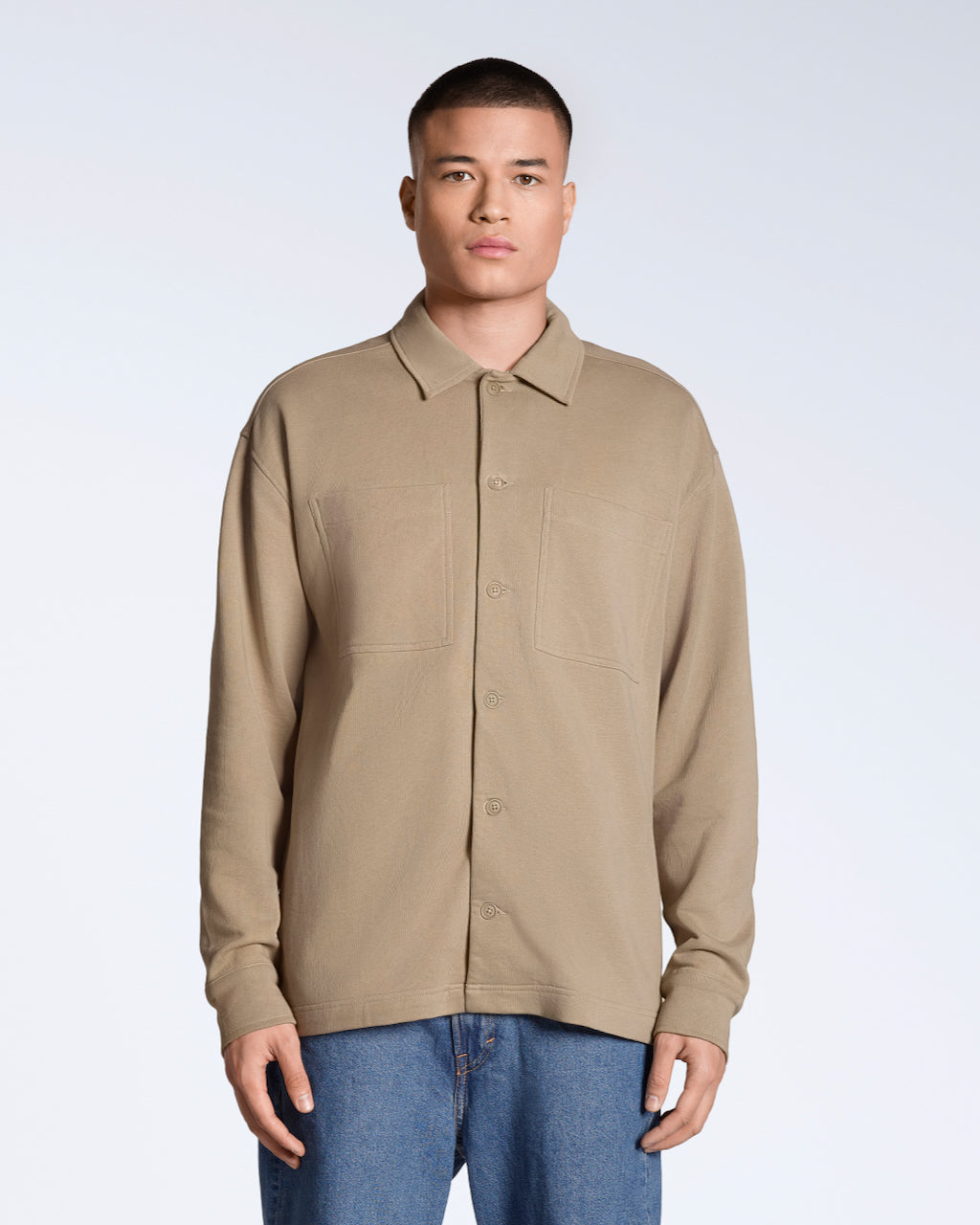 A man facing front on looking into the camera, modelling a plain beige, organic cotton overshirt.
