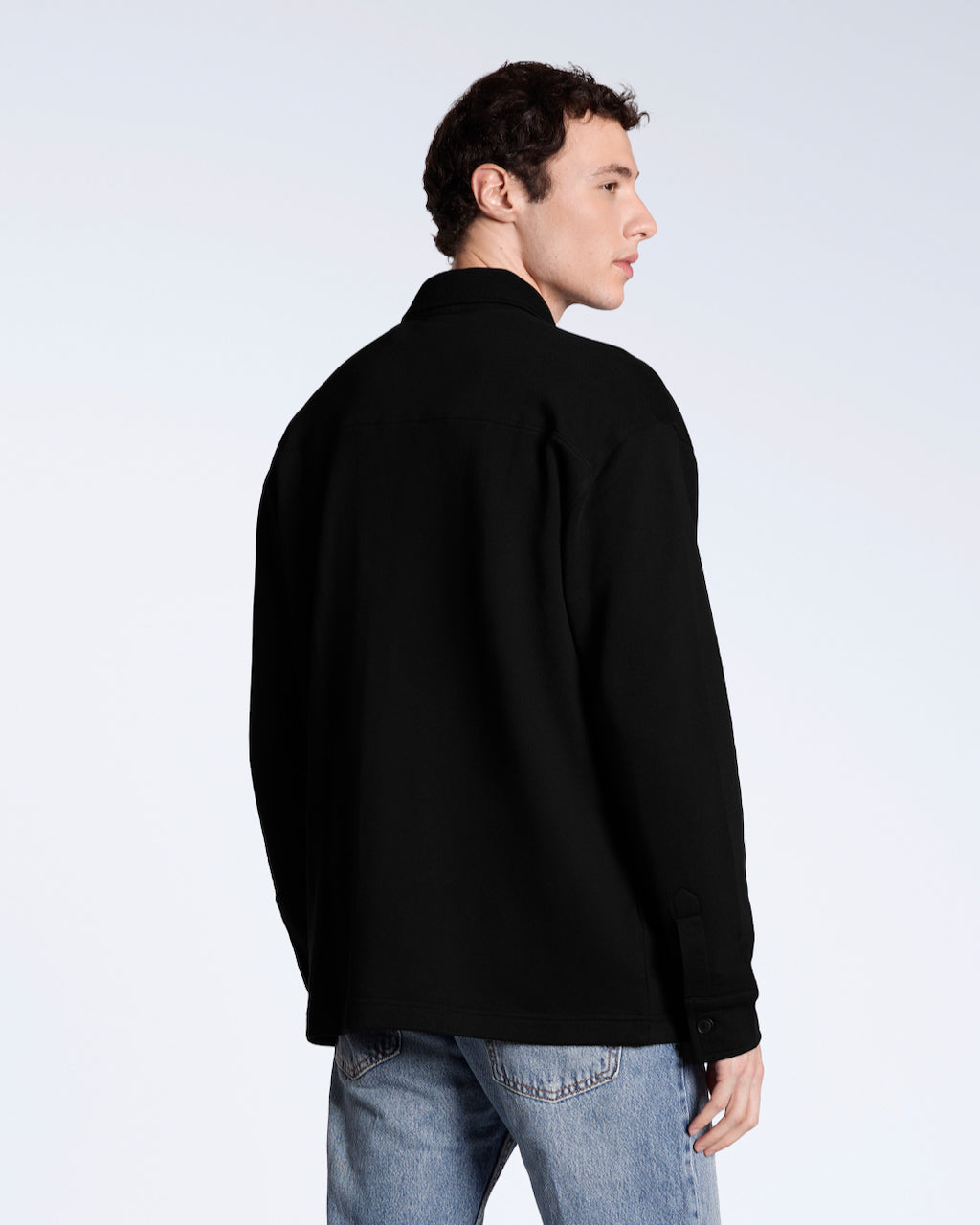 A man facing away from the camera, modelling a plain black, organic cotton overshirt.