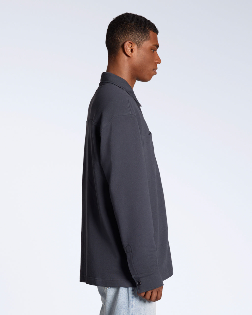 A man facing side on, modelling a plain dark grey, organic cotton overshirt.