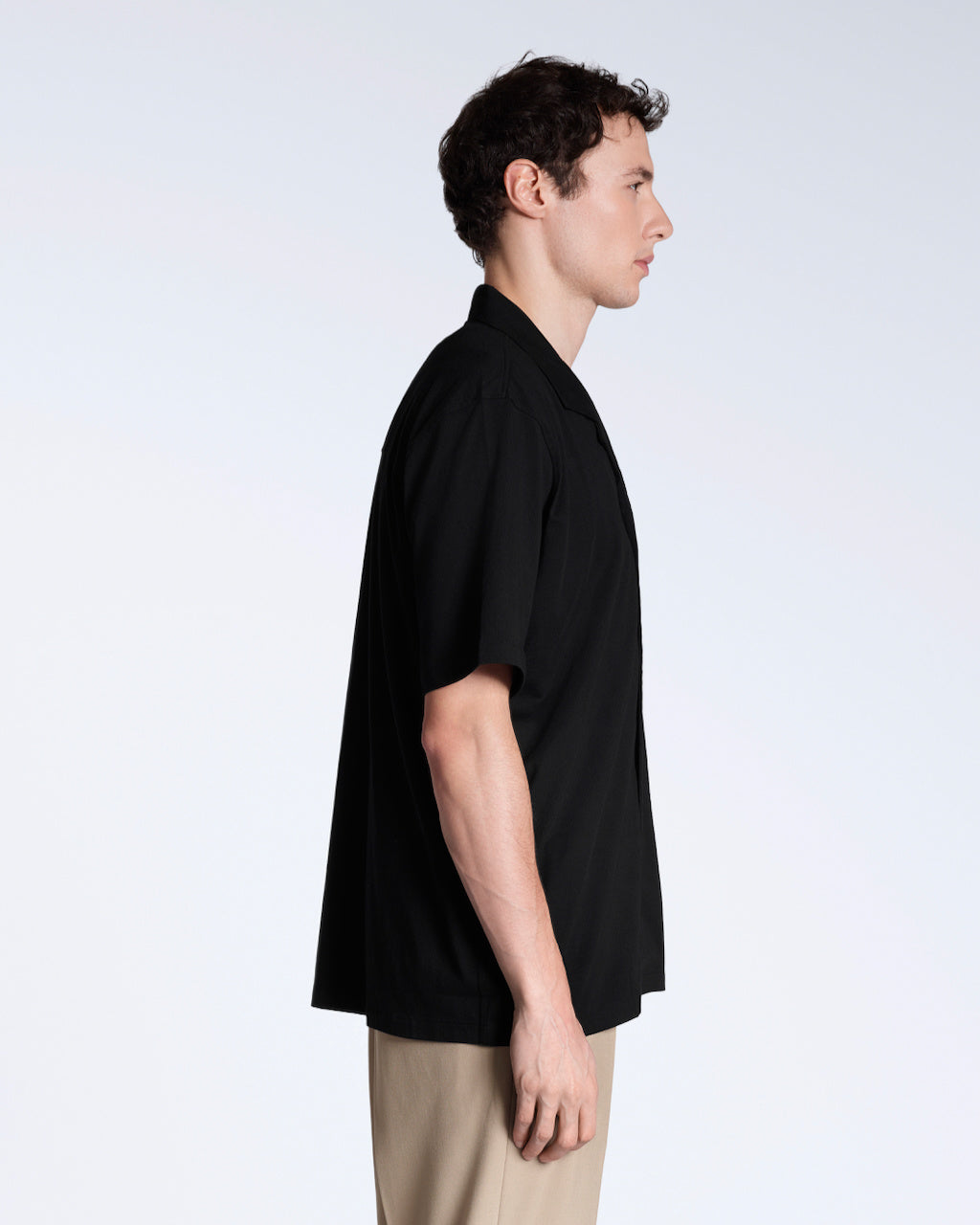 A man facing side on, modelling a plain black, organic cotton resort shirt.