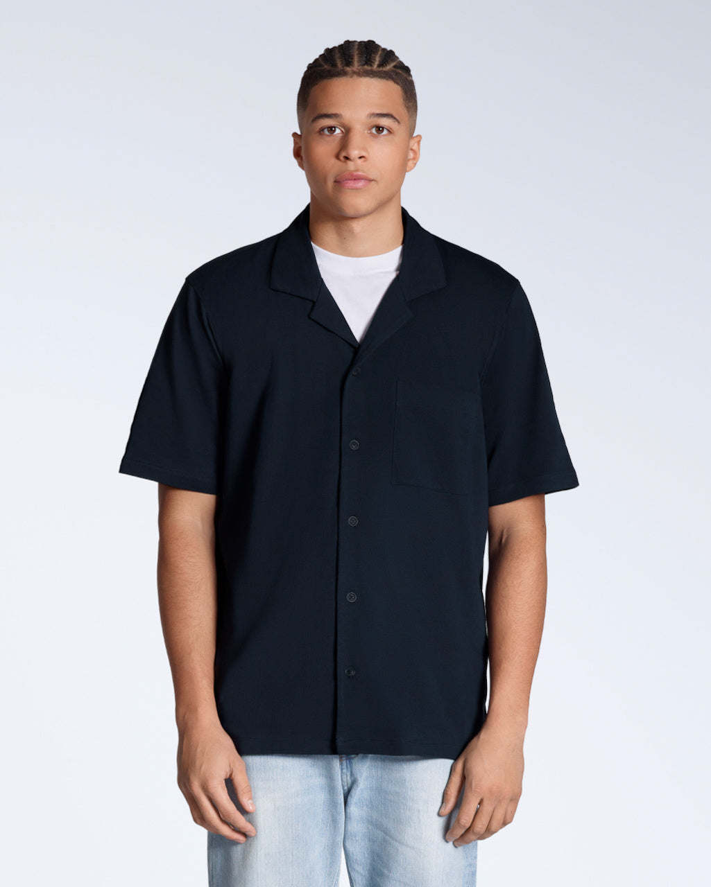 A man facing front on looking into the camera, modelling a plain navy, organic cotton resort shirt.