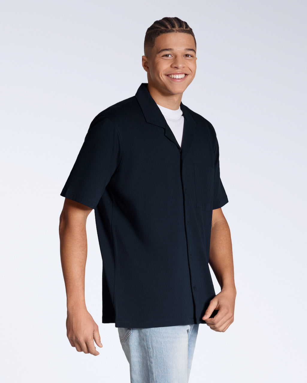 A man smiling into the camera, modelling a plain navy, organic cotton, short sleeve resort shirt.