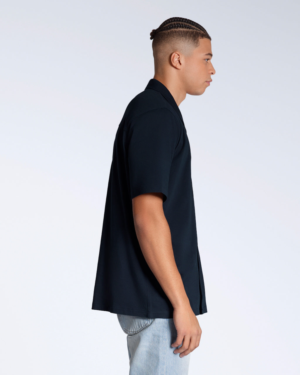A man facing side on, modelling a plain navy, organic cotton resort shirt.