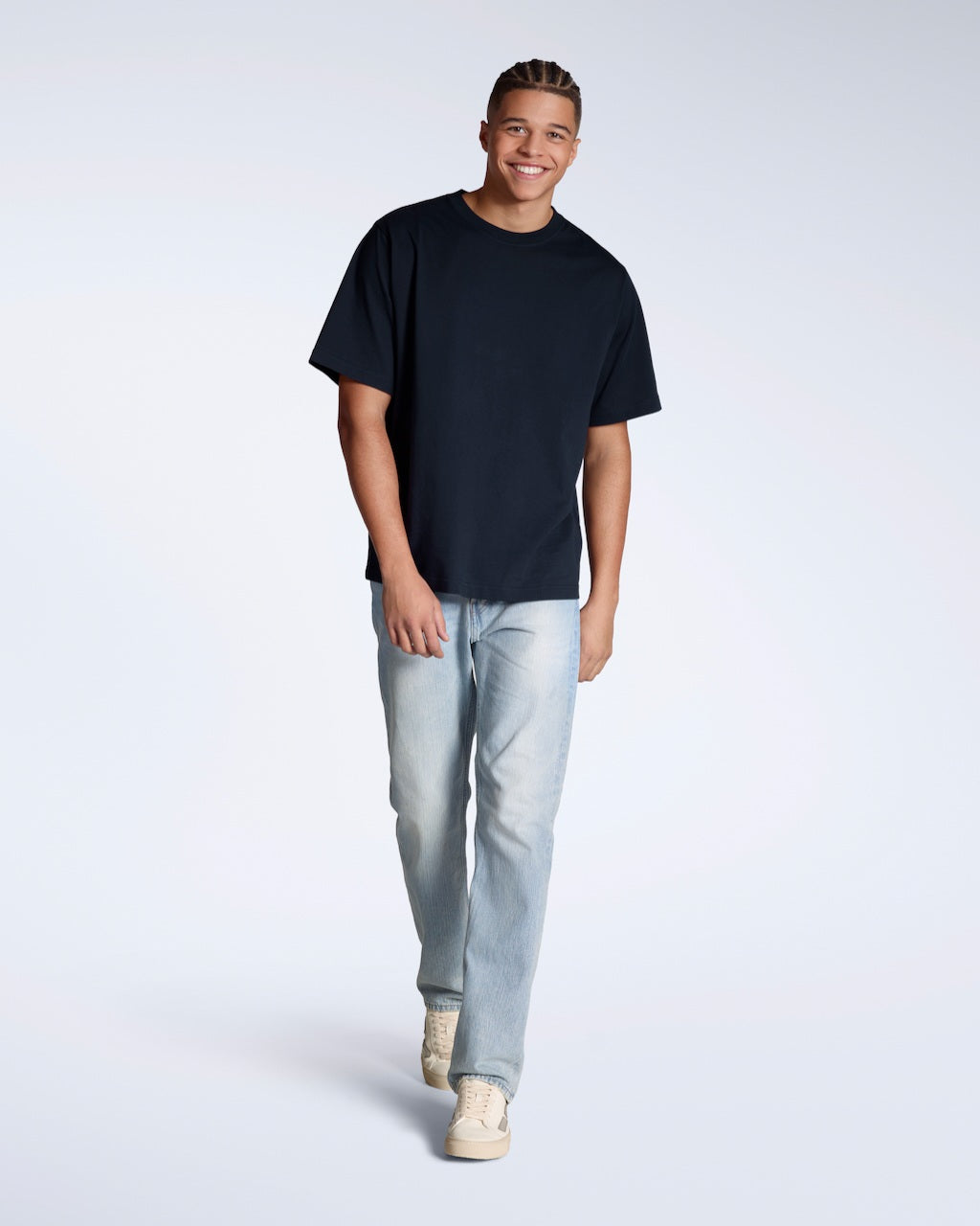 A full body photo of a man smiling, walking towards the camera, modelling a plain navy, oversized, organic cotton t shirt.