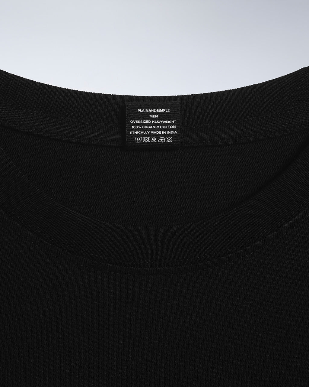 A close up of an neck label in a men's black oversized heavyweight organic cotton t shirt.