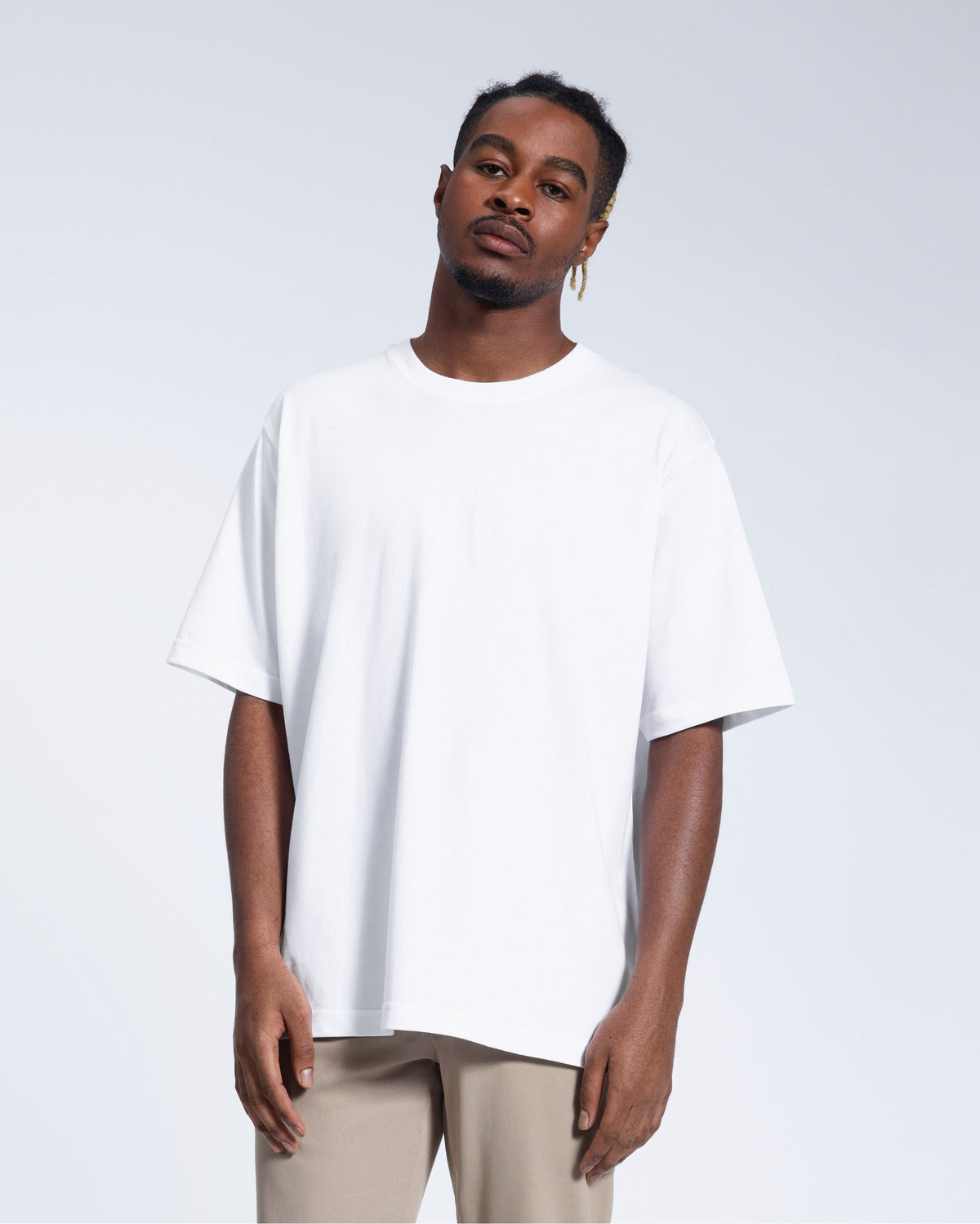 A man face on looking into the camera with his arms by his side, modelling a plain white oversized heavyweight organic cotton t shirt.