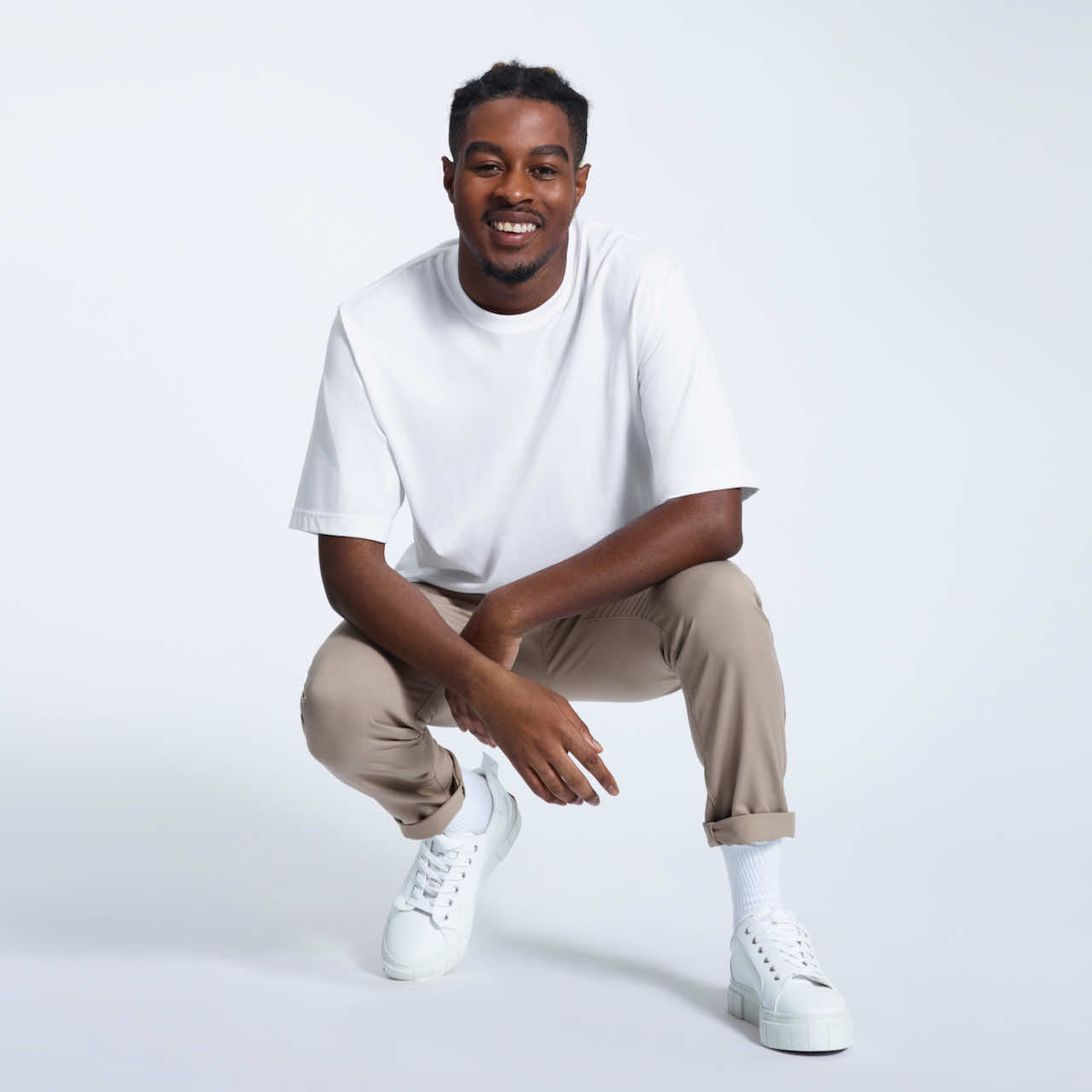 A man kneeling down smiling, modelling a plain white oversized heavyweight organic cotton t shirt.