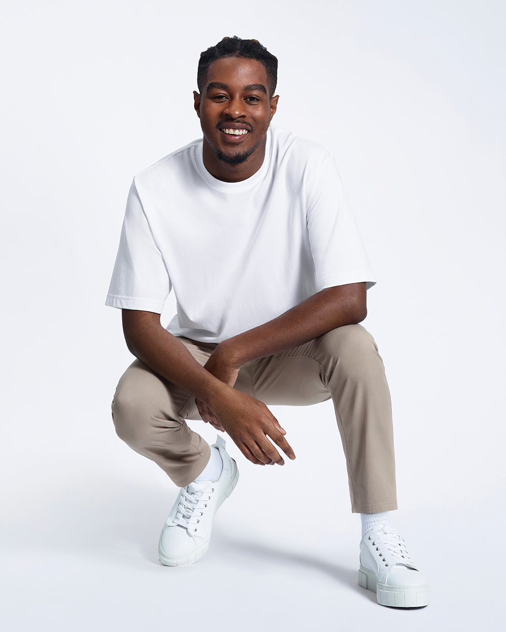 A man kneeling down smiling, modelling a plain white oversized heavyweight organic cotton t shirt.