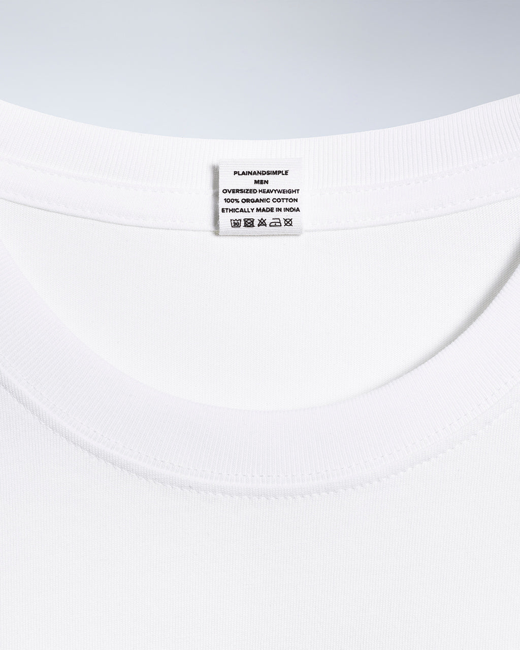 A close up of an neck label in a men's white oversized heavyweight organic cotton t shirt.