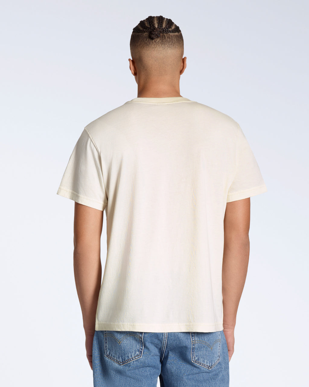 A man facing away from the camera, modelling a plain, natural coloured, short sleeve organic cotton t shirt.