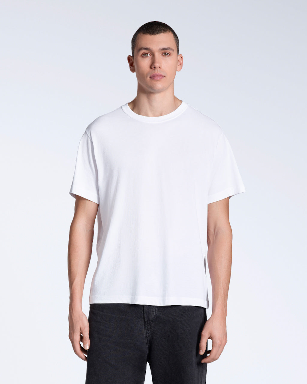 A man facing front on looking into the camera, modelling a plain white, organic cotton t shirt.