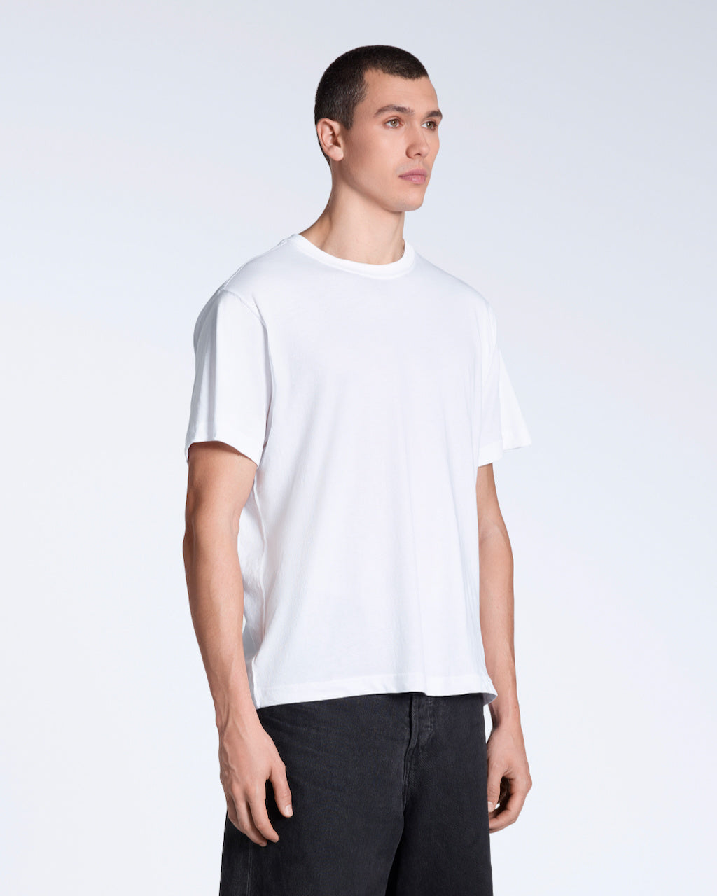 A man at an angle with his arms by his sides, modelling a plain white, short sleeve organic cotton t shirt.