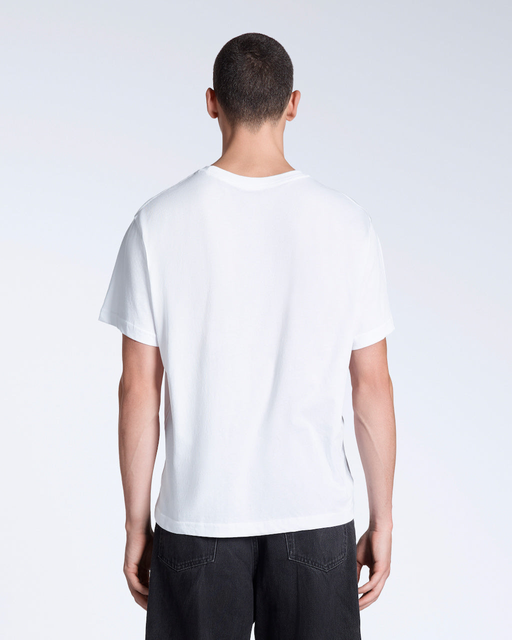 A man facing away from the camera, modelling a plain white, short sleeve organic cotton t shirt.