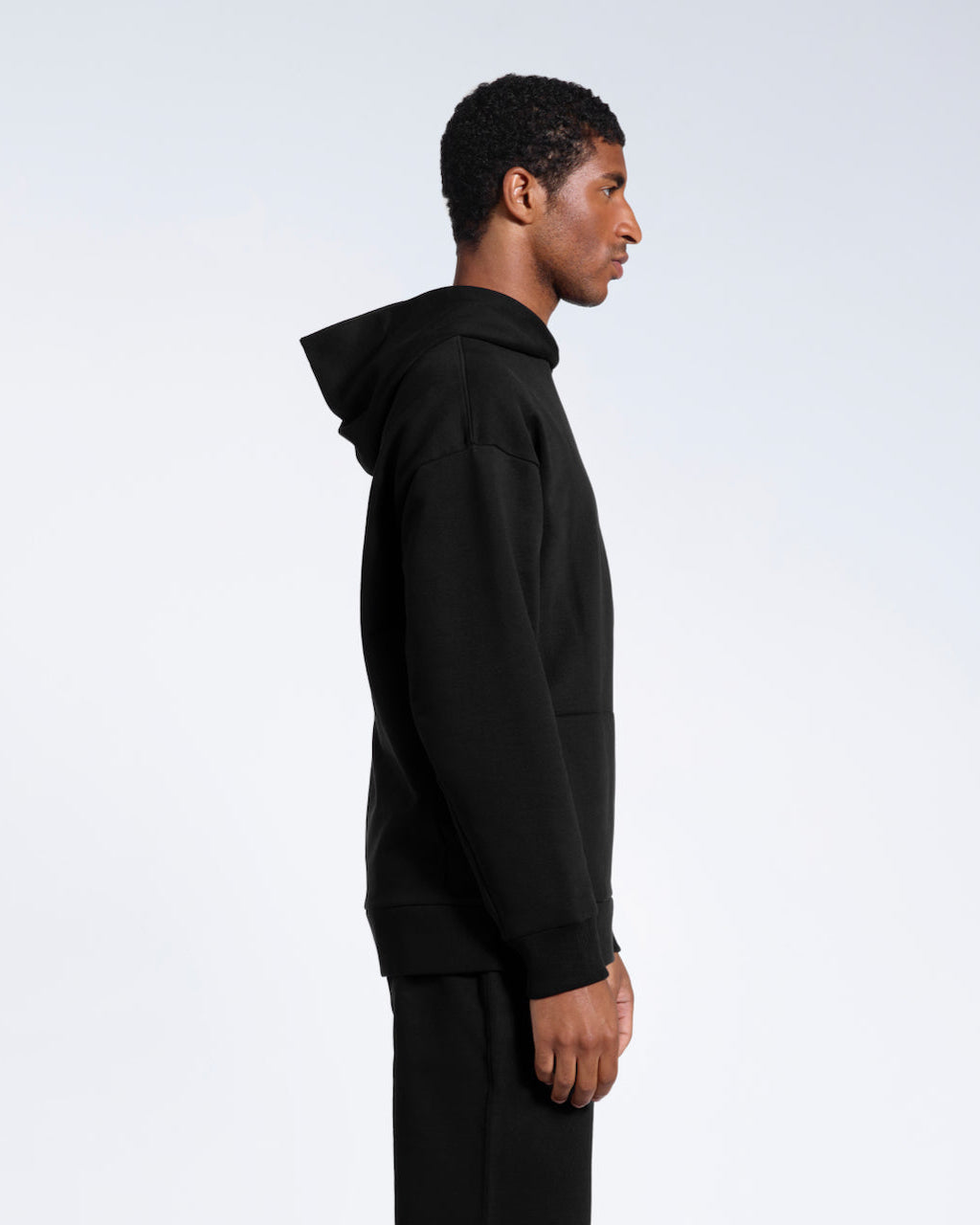 A man facing side on, modelling a black oversized organic cotton hoodie.