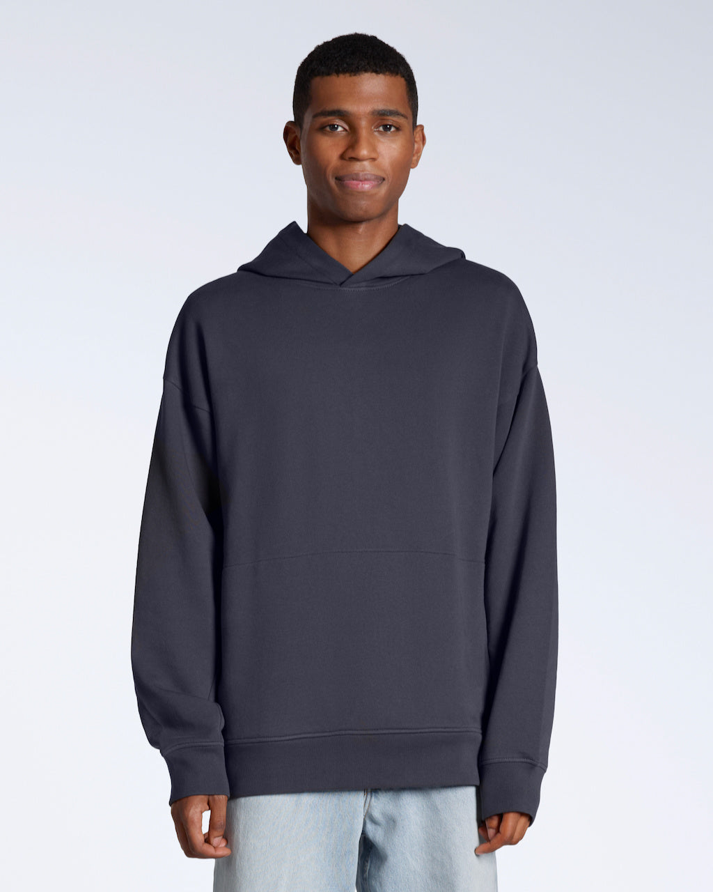 A man facing front on looking into the camera with his arms by his sides, modelling a dark grey oversized organic cotton hoodie.