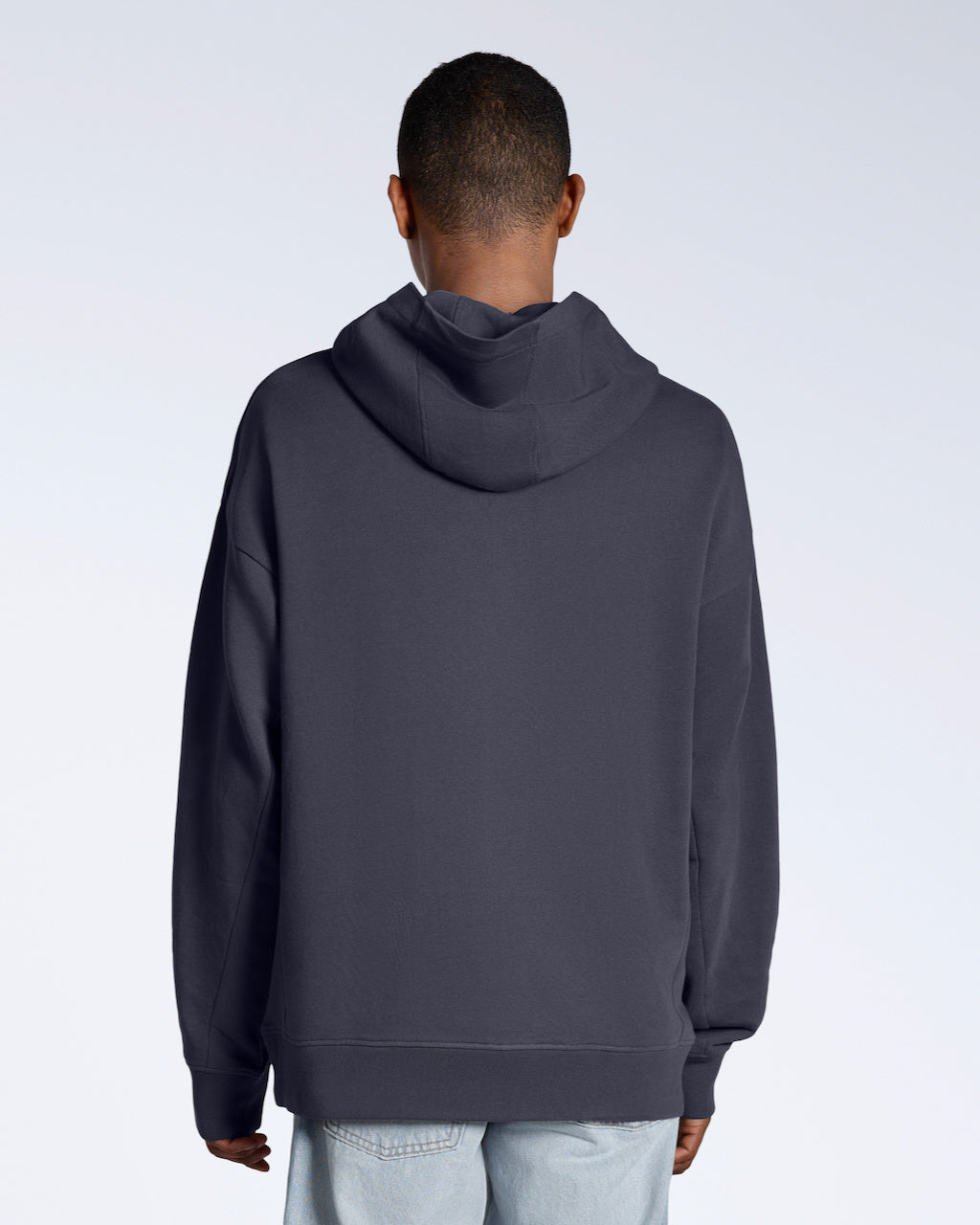 A man facing away from the camera with his arms by his sides, modelling a dark grey oversized organic cotton hoodie.