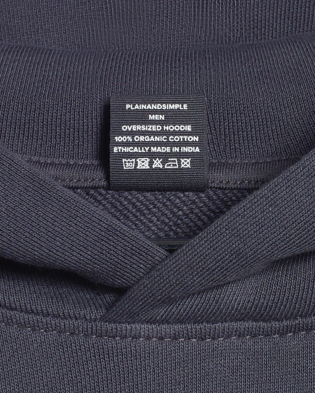 A close up of the neck label in a dark grey, oversized, organic cotton hoodie.