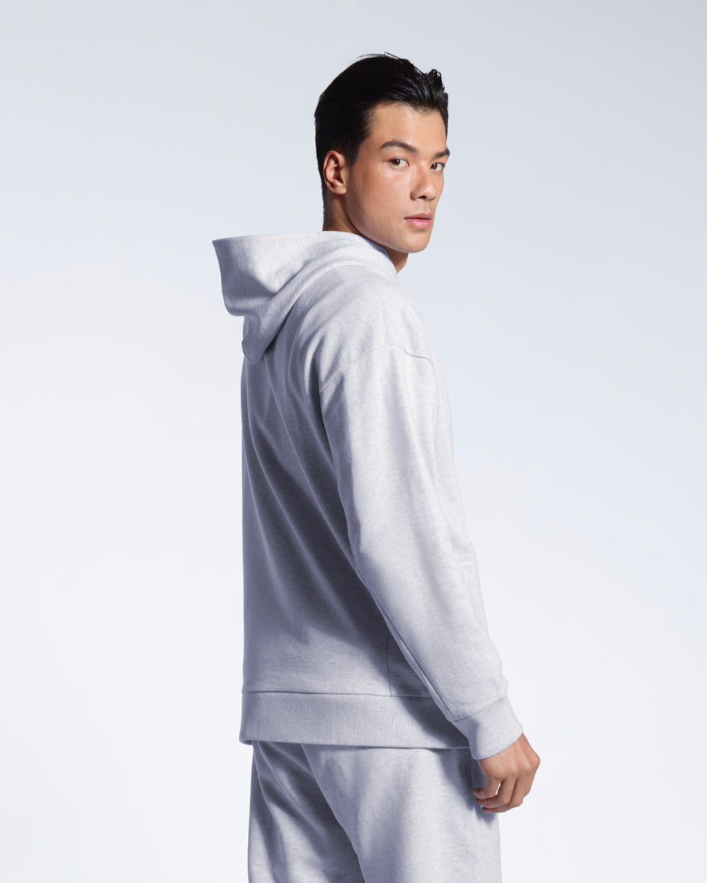 A man looking back at the camera, showing the back of his grey oversized organic cotton hoodie with matching joggers.