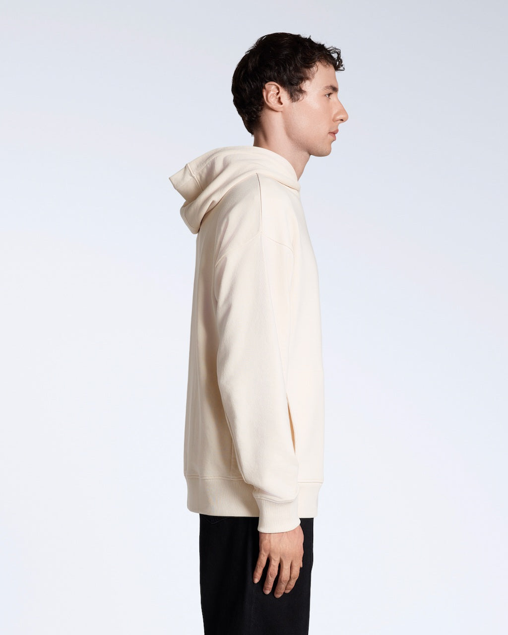 A man facing side on, modelling a natural coloured oversized organic cotton hoodie.