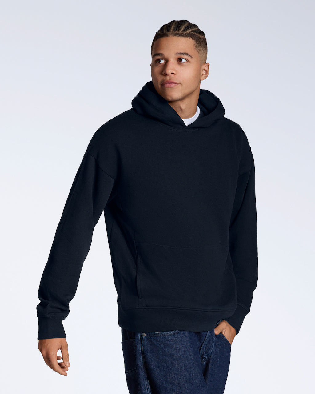 A man looking away from the camera with a hand in his pocket, modelling a navy oversized organic cotton hoodie.