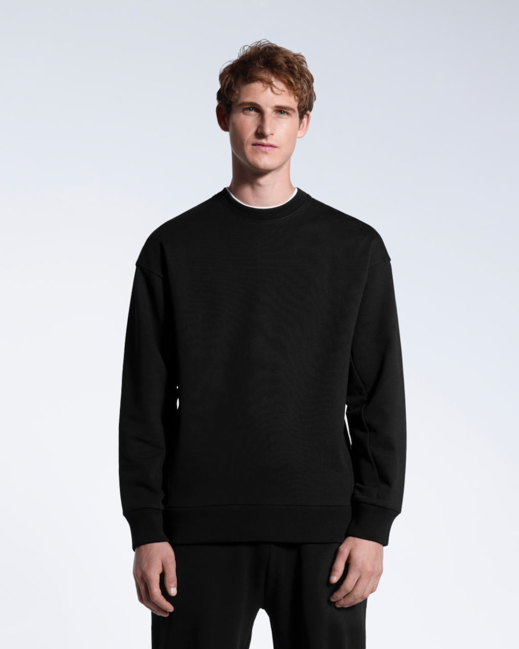 A man face on with his arms by his side, modelling a black oversized organic cotton sweatshirt.