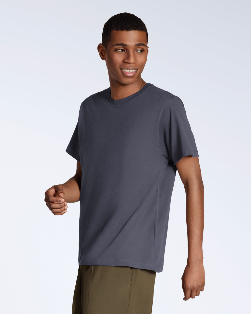 A man smiling looking away from the camera, modelling a plain dark grey, organic cotton t shirt.
