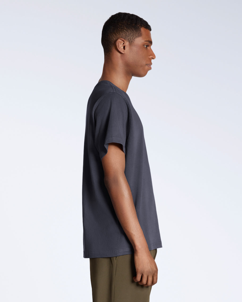 A man facing side on, modelling a plain dark grey short sleeve organic cotton t shirt.