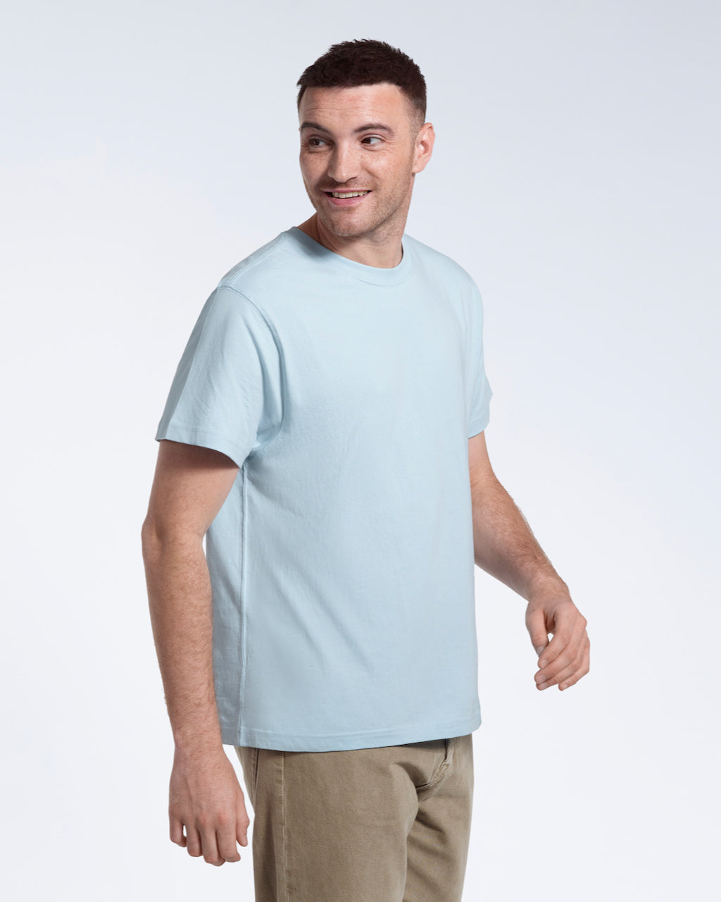 A man smiling looking back, modelling a plain light blue short sleeve organic cotton t shirt.