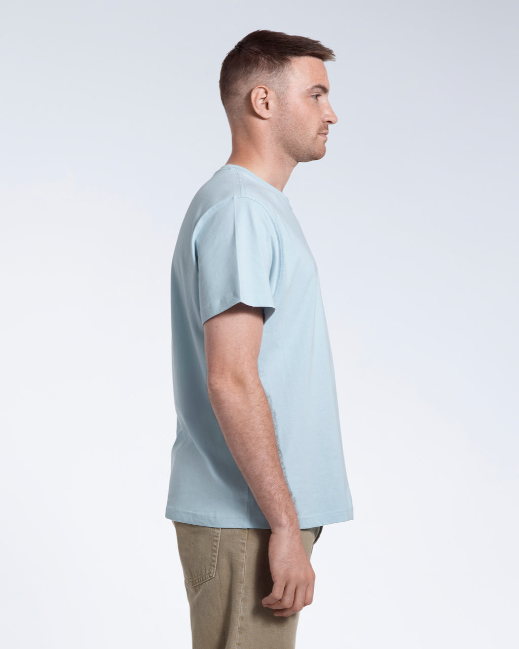 A man facing side on, modelling a plain light blue short sleeve organic cotton t shirt.