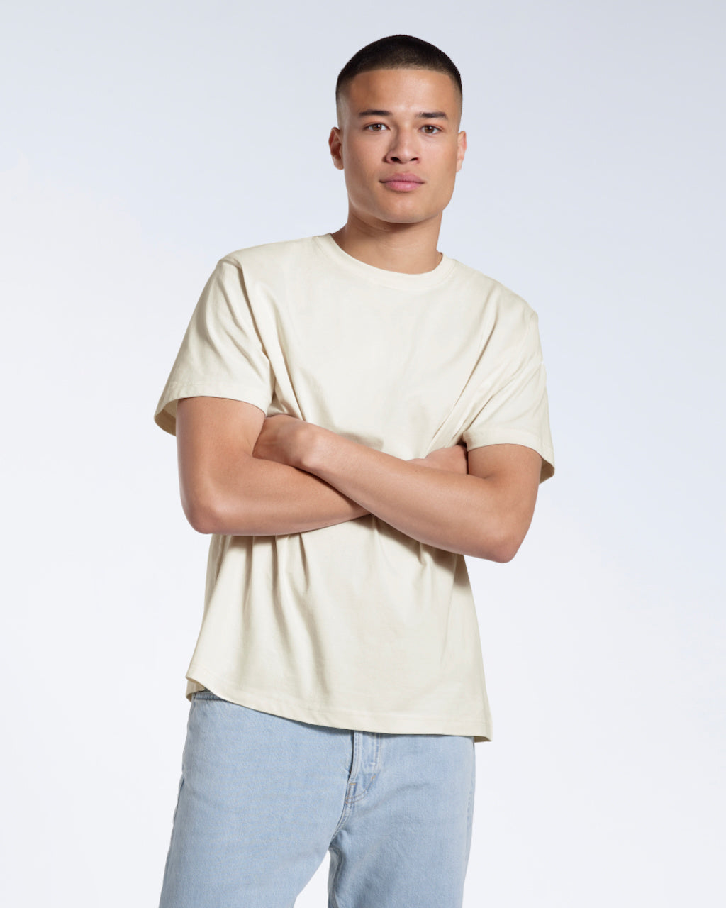 A man looking into the camera with his arms crossed, modelling a plain ecru short sleeve organic cotton t shirt.