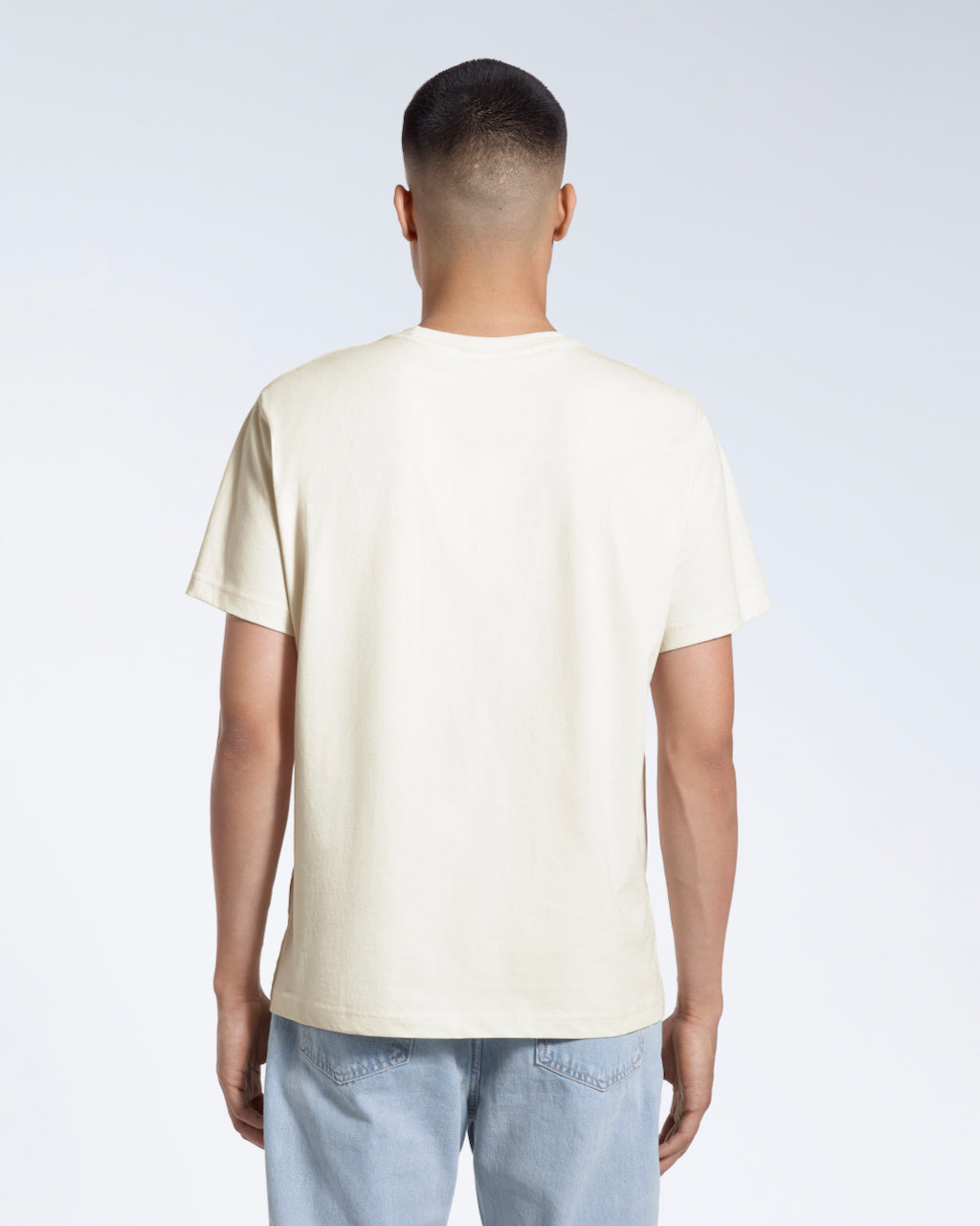 A man facing away from the camera, modelling a plain ecru short sleeve organic cotton t shirt.
