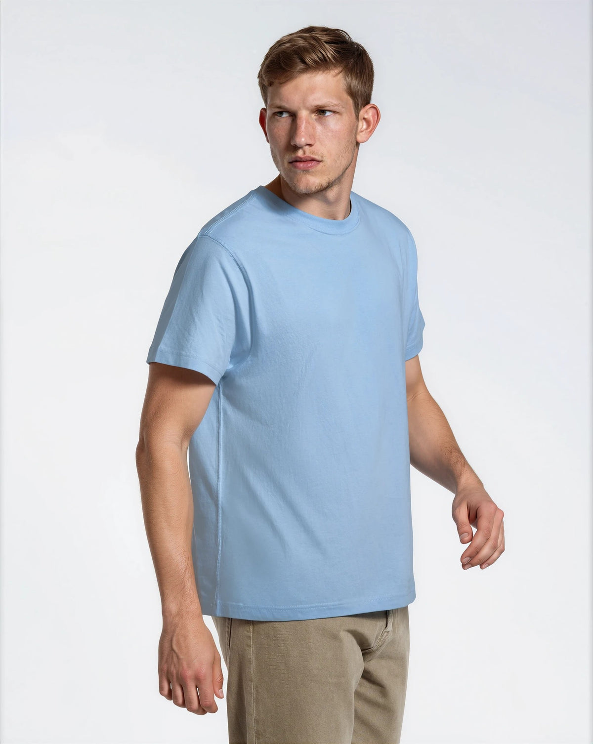 A man looking away from the camera, modelling a plain blue, organic cotton t shirt.