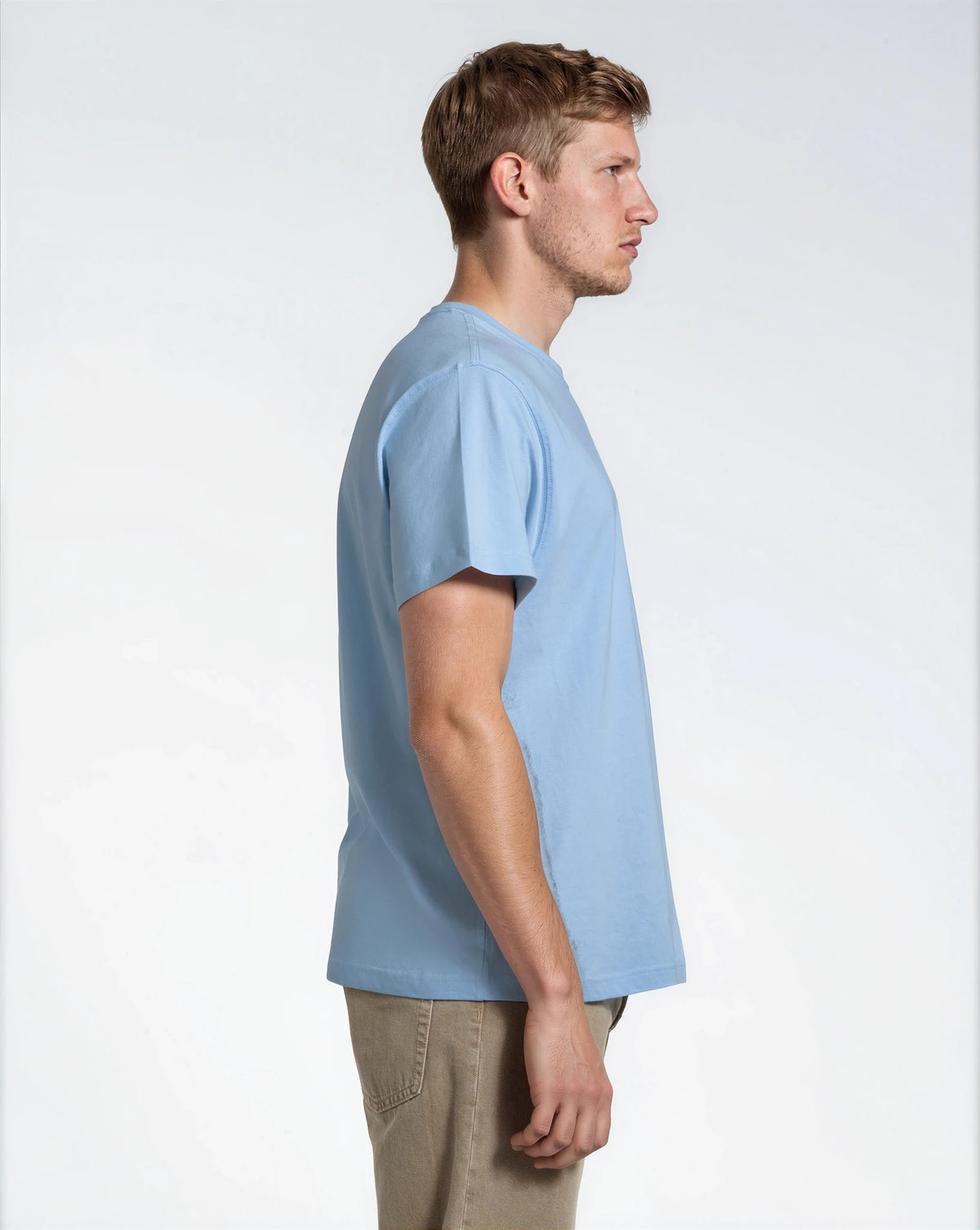 A man facing side on, modelling a plain blue, short sleeve organic cotton t shirt.