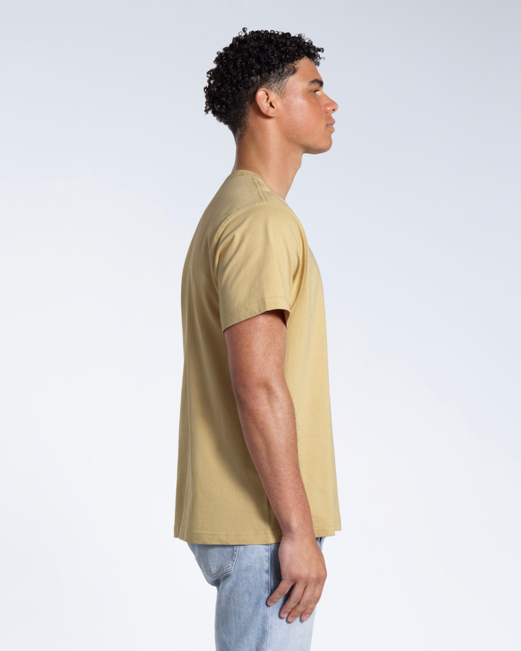 A man facing side on, modelling a plain light khaki short sleeve organic cotton t shirt.