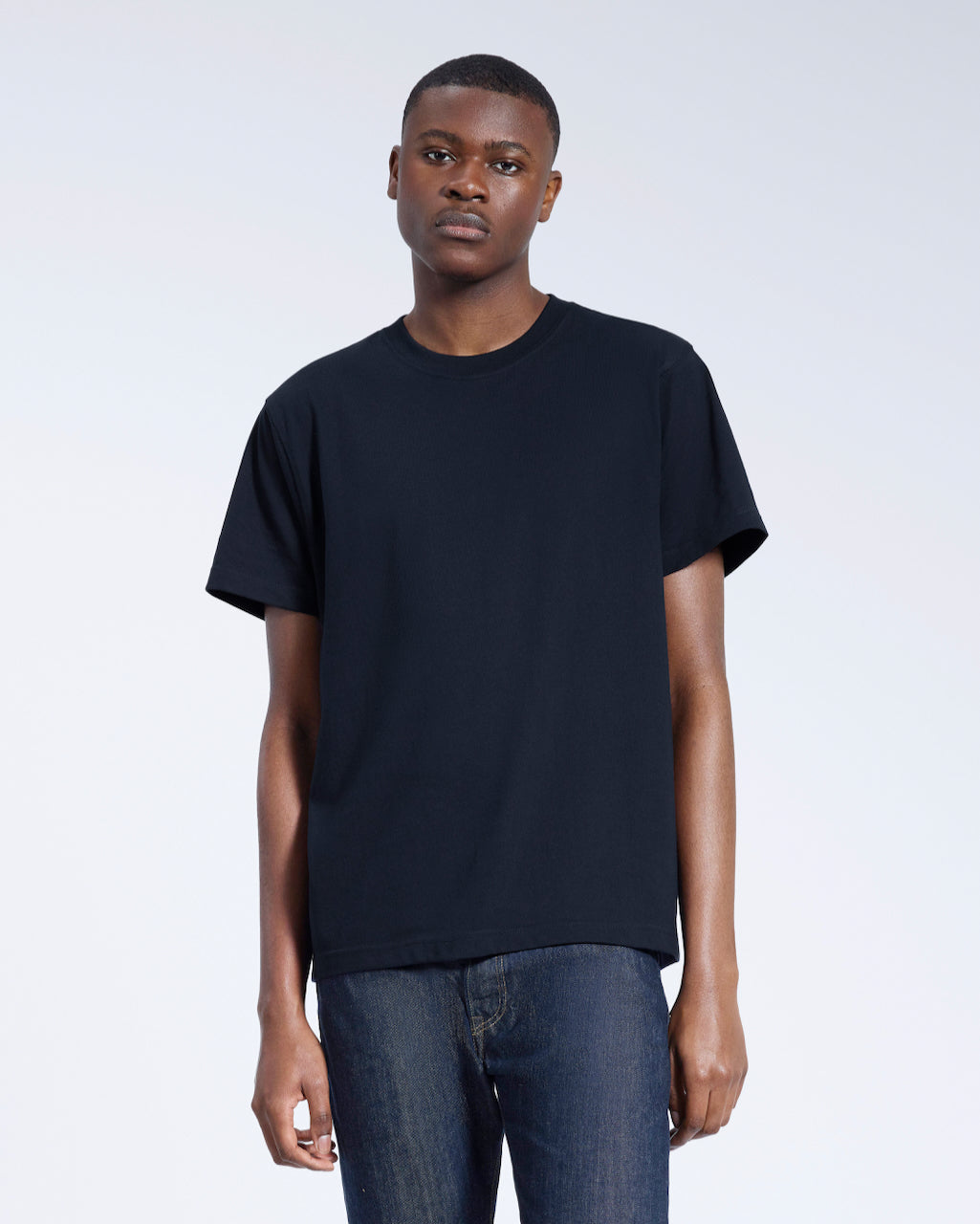 A man facing front on looking into the camera, modelling a plain navy, organic cotton t shirt.