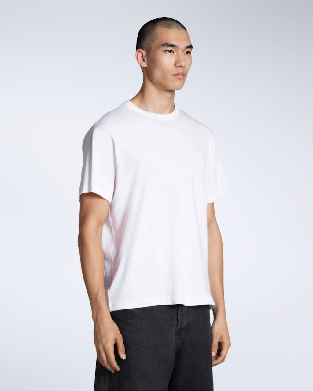 A man at an angle with his arms by his sides, modelling a plain white, short sleeve organic cotton t shirt.
