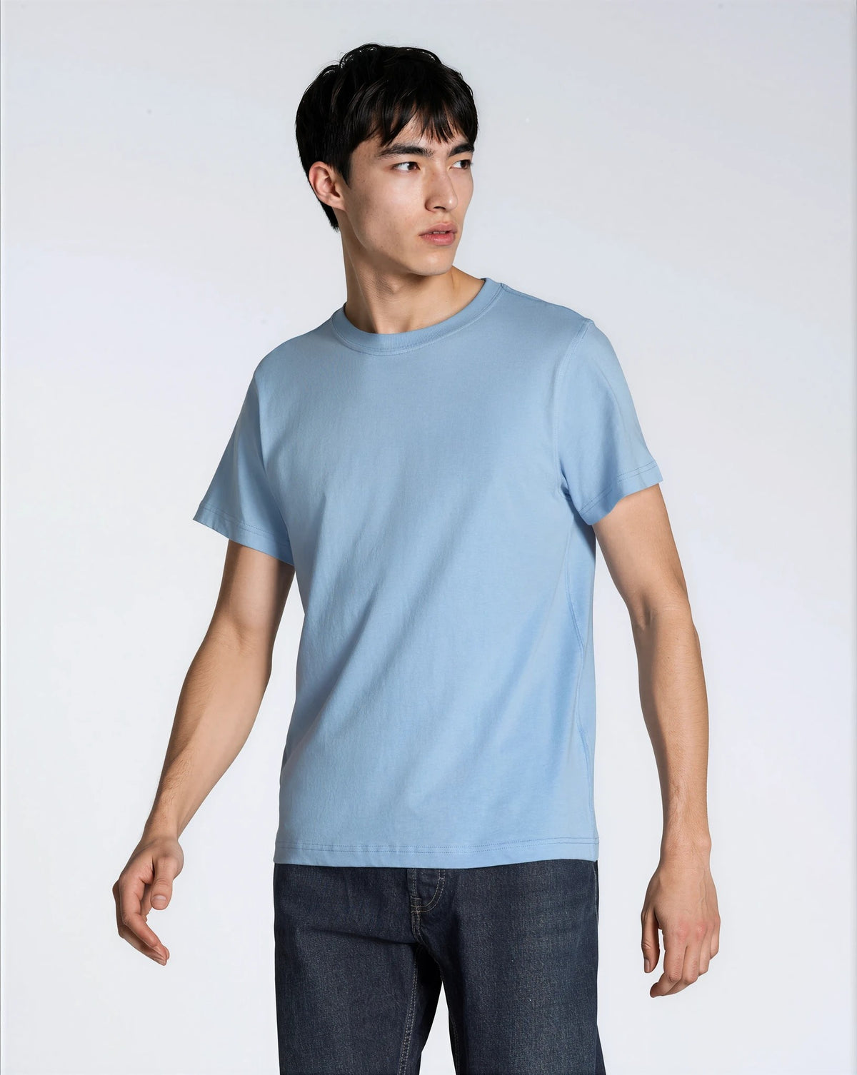 A man looking away from the camera, modelling a plain blue, organic cotton t shirt.