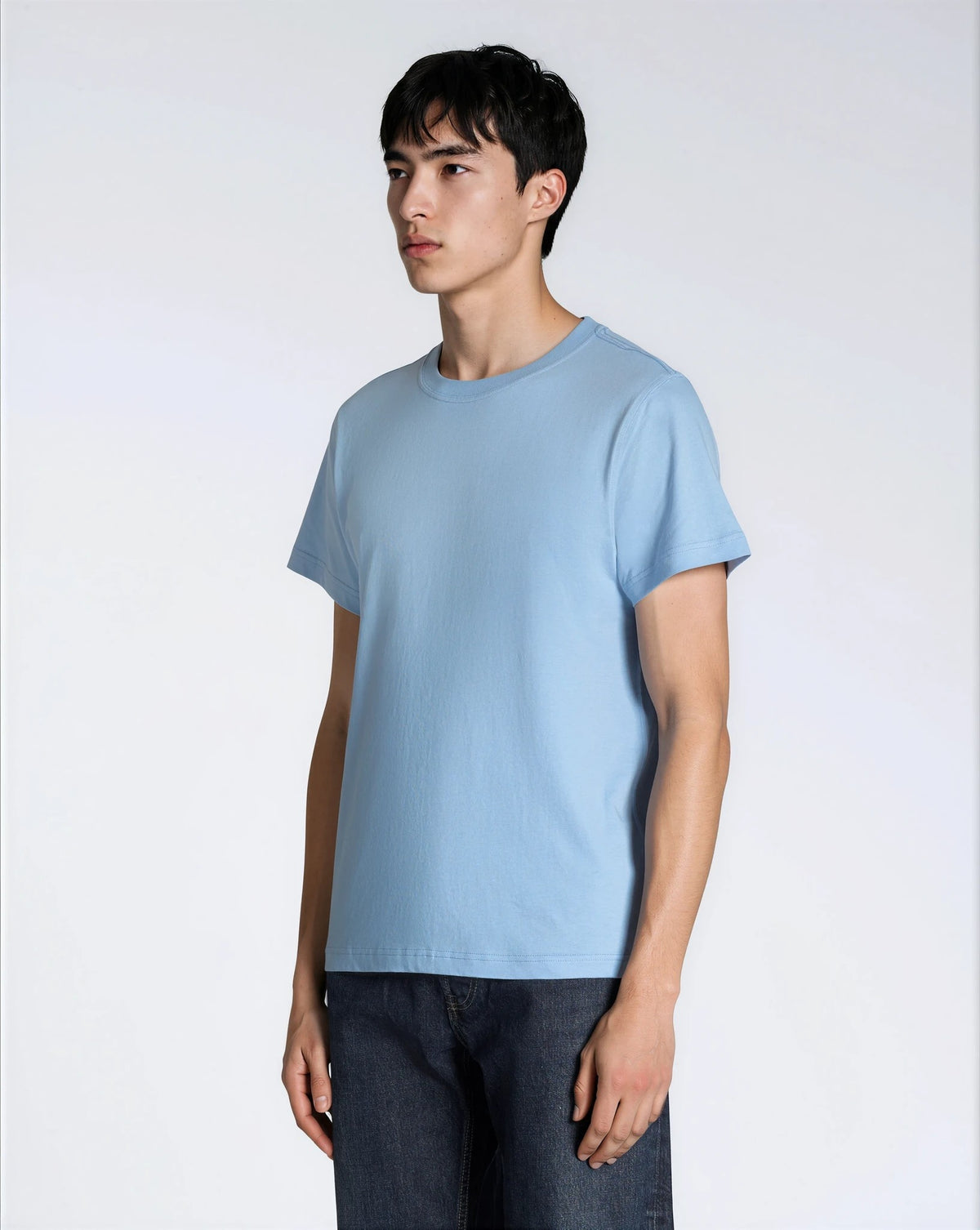 A man at an angle with his arms by his sides, modelling a plain blue short sleeve organic cotton t shirt.