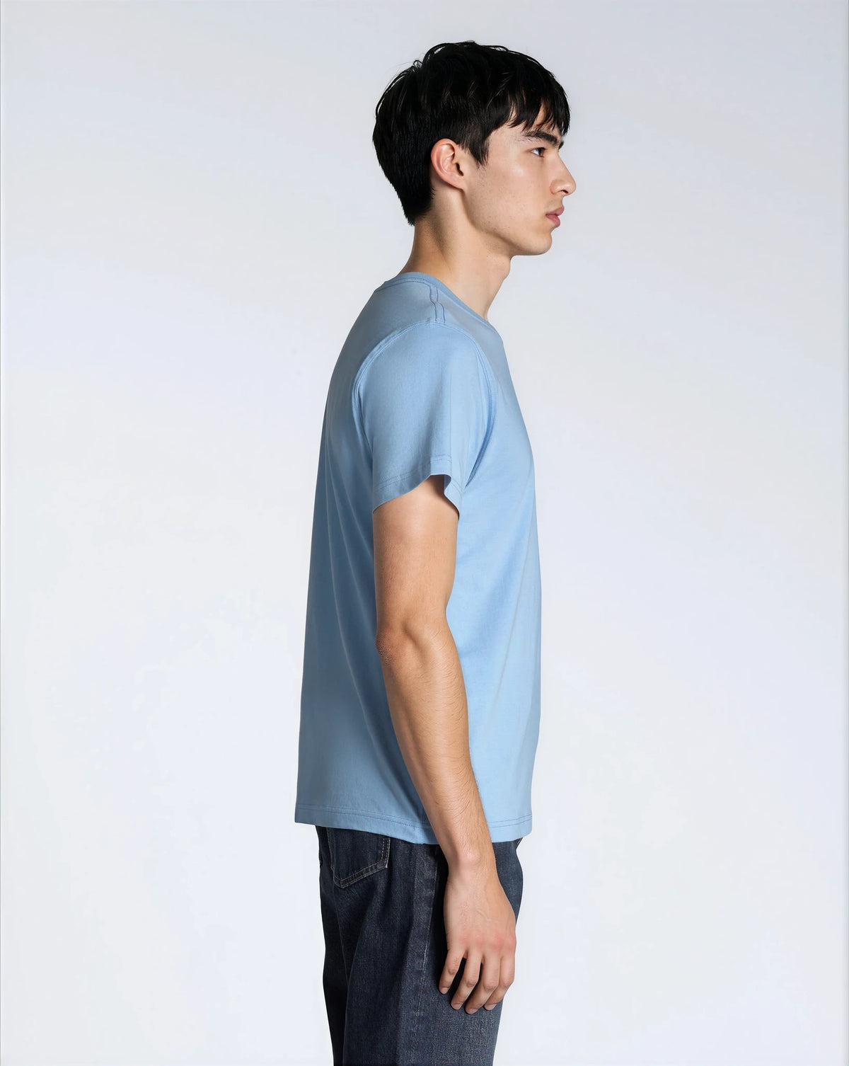 A man facing side on, modelling a plain blue short sleeve organic cotton t shirt.