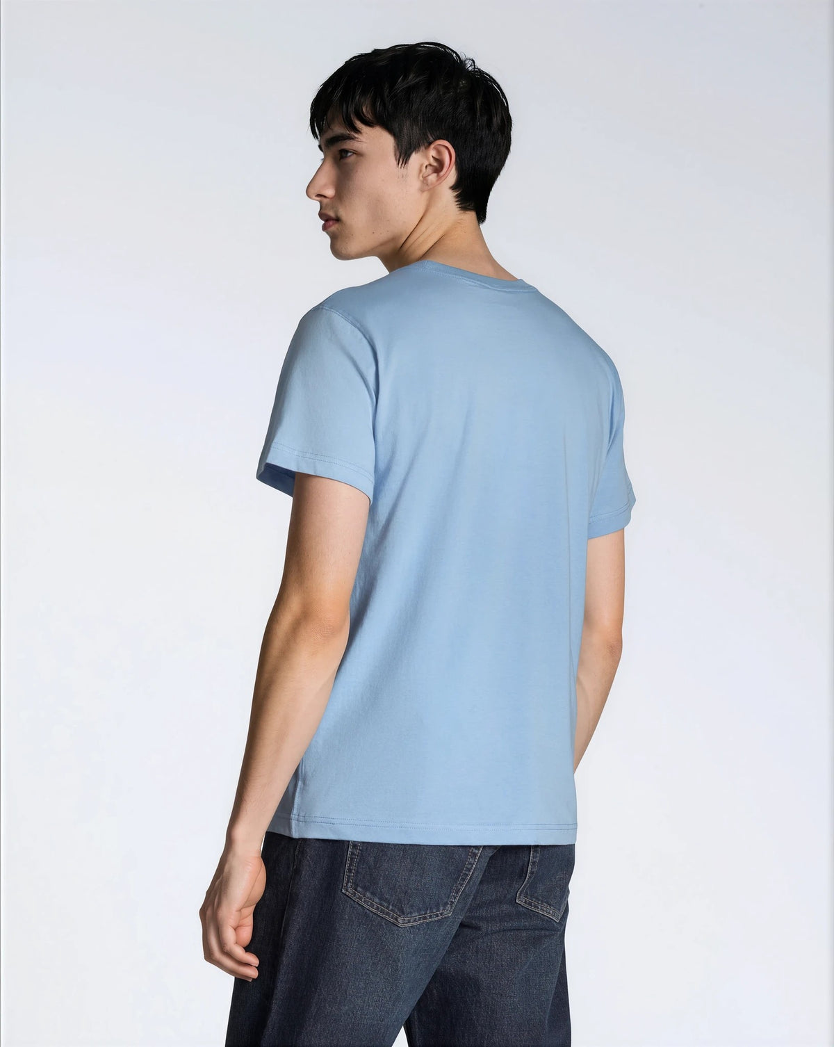 A man facing away from the camera, modelling a plain blue short sleeve organic cotton t shirt.